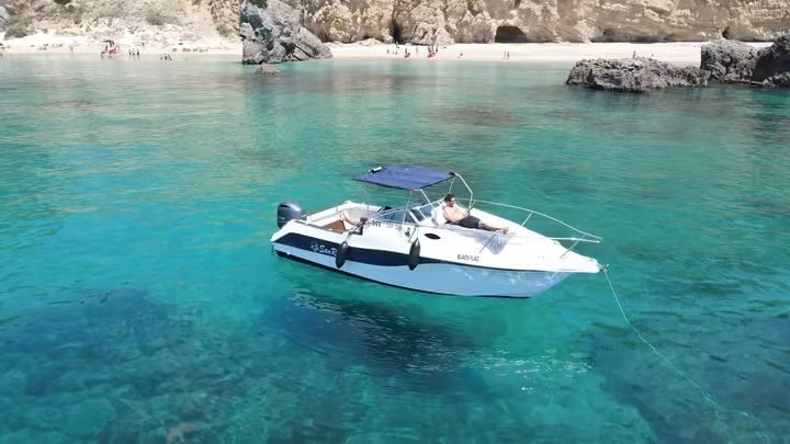 Barco Black Flag fundeado em água turquesa junto à praia e às falésias