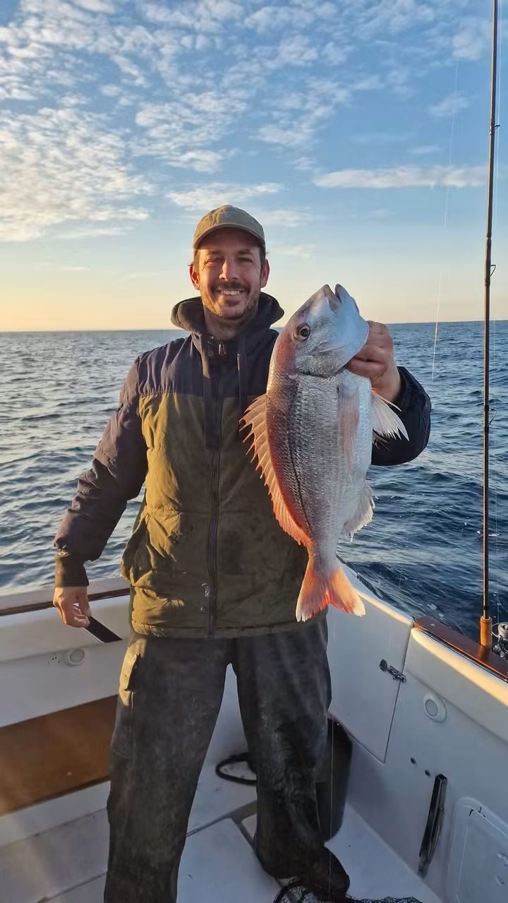 Pescador com um pargo grande a bordo ao pôr do sol